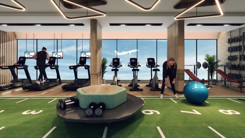 Modern gym with cardio machines, weight training equipment, and functional training area. People exercising on treadmills, stationary bikes, and with fitness balls. Large windows offer natural light and views of the sky, creating a bright and motivating workout environment.