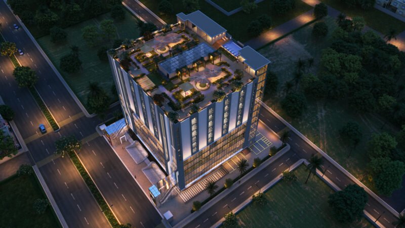 Aerial nighttime view of NRI Avenue, a modern multi-story building with illuminated exterior and rooftop garden. The building is surrounded by roads and greenery, with well-lit streets and parking areas, showcasing contemporary architecture and urban planning.